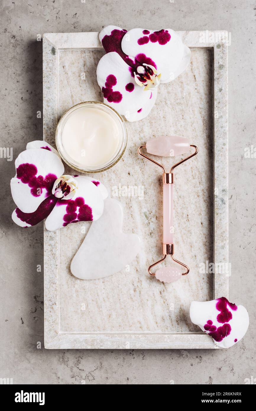 Rouleau à cadran en quartz rose, fleurs de SHA gua et d'orchidées sur fond de marbre. Concept spa, soin du visage. Banque D'Images
