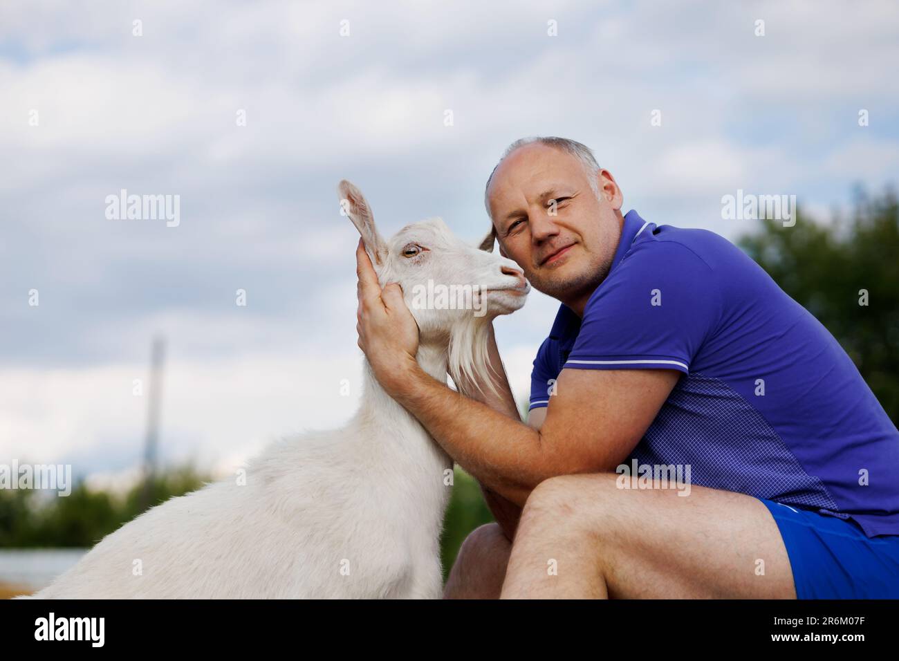 un homme d'âge moyen parle face à face à une chèvre blanche et sourit Banque D'Images