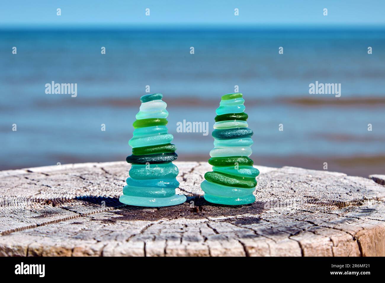 Deux pyramides équilibrées de fragments humides et polies de la mer d'une bouteille en verre bleu et vert sur un tronc en bois abîmé coupé contre la mer Banque D'Images
