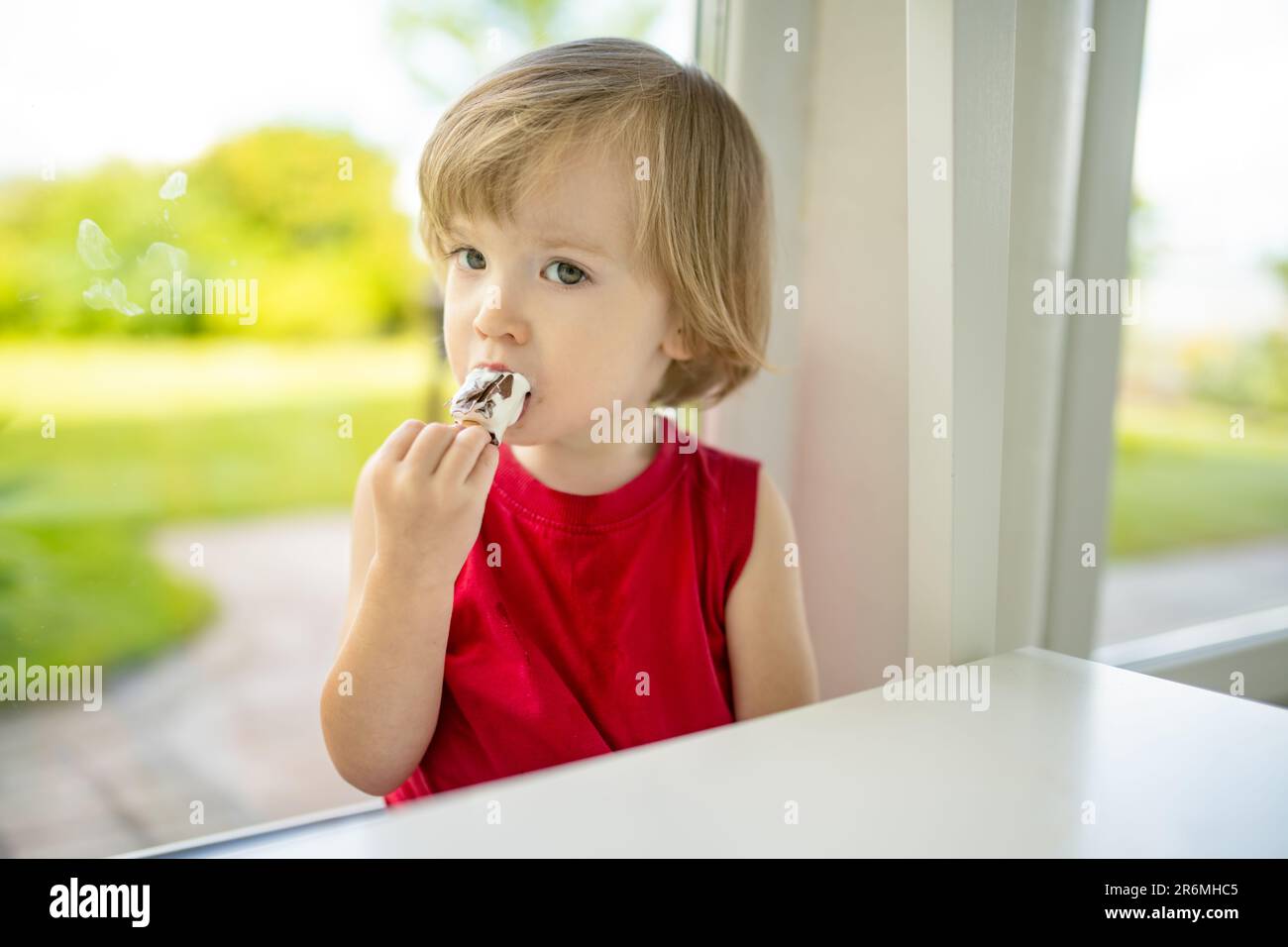 Un tout-petit mignon qui mange de la glace fraîche savoureuse à la maison. Les enfants mangeant des bonbons. Nourriture malsaine pour les enfants. Banque D'Images