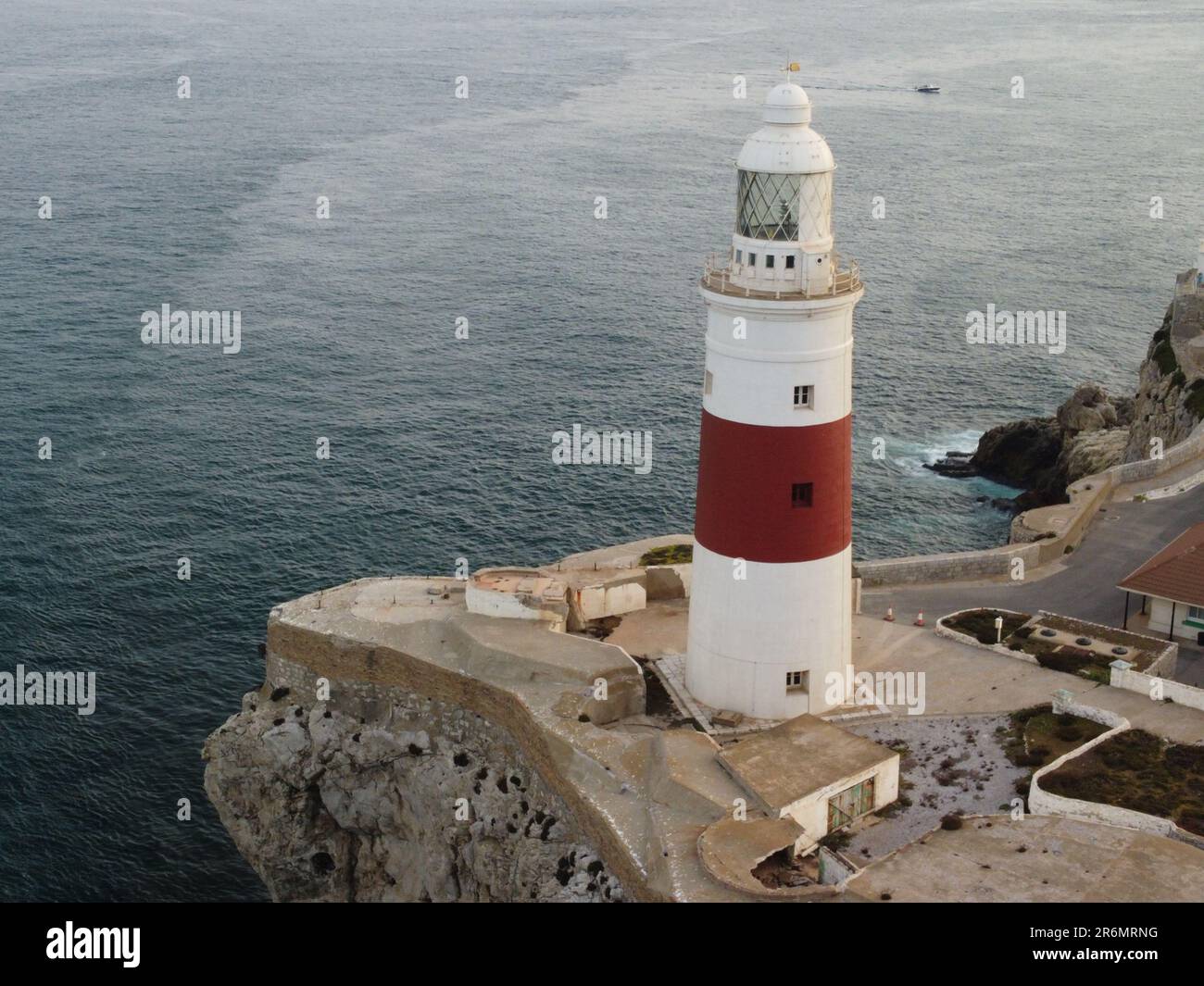 Un paysage côtier pittoresque avec un phare rouge et blanc vivant situé à côté d'un océan bleu tranquille avec plusieurs petits bateaux dans l'eau Banque D'Images