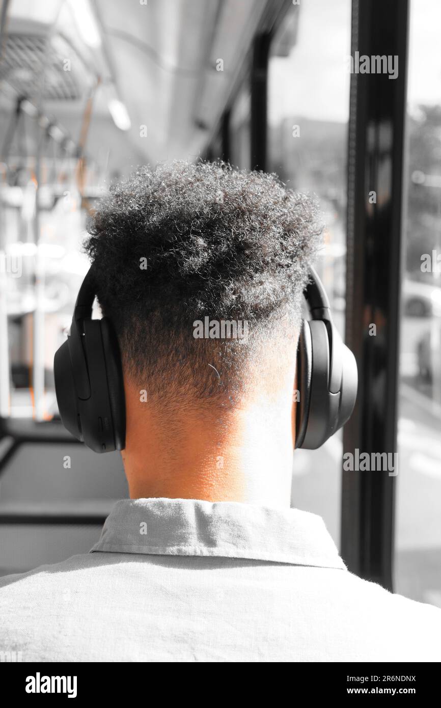 Un homme avec une coupe de cheveux moderne portant des écouteurs dans le bus public Banque D'Images