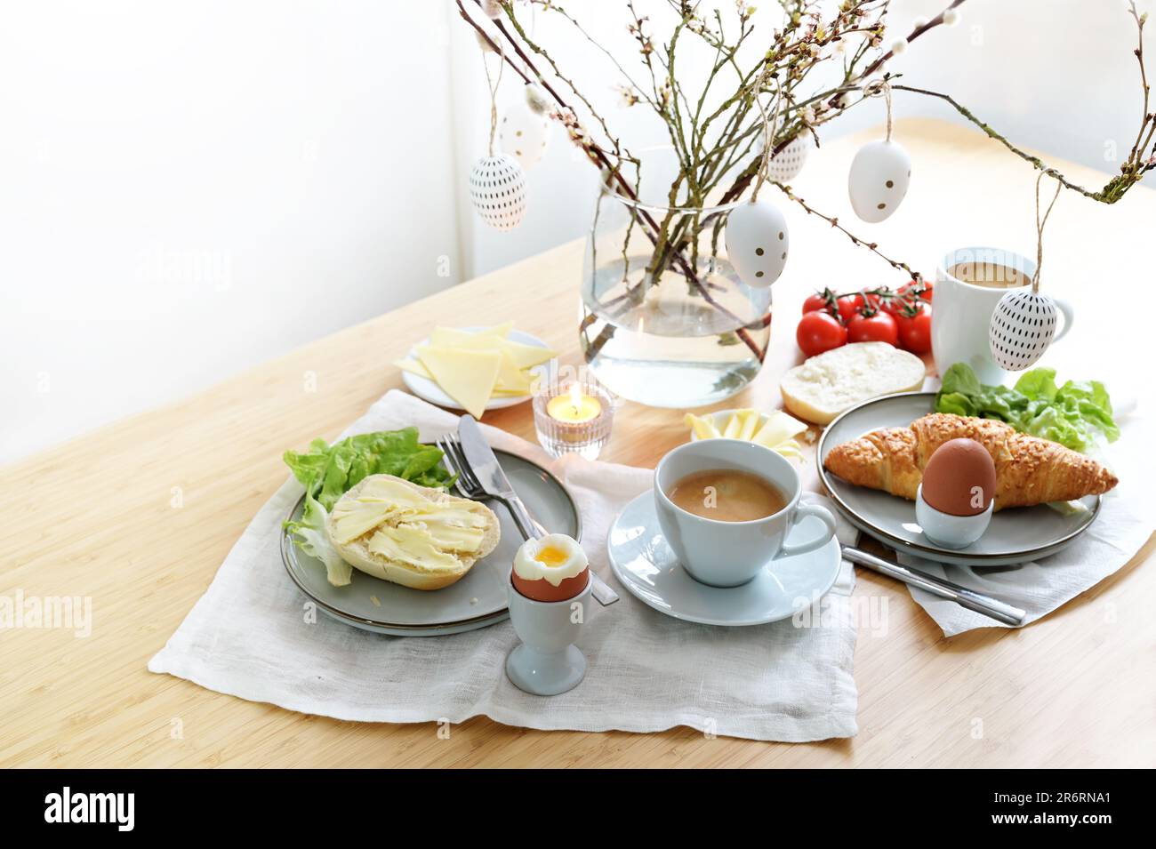 Petit-déjeuner de Pâques avec pain, fromage et œuf décoré de branches de printemps et d'œufs de pâques suspendus dans un vase en verre sur une table à manger, c Banque D'Images