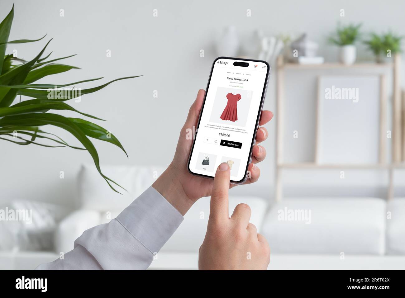 Femme magasiner en ligne avec un smartphone. Acheter une robe rouge de flux sur la page Web d'ecommerce. Intérieur du salon en arrière-plan Banque D'Images