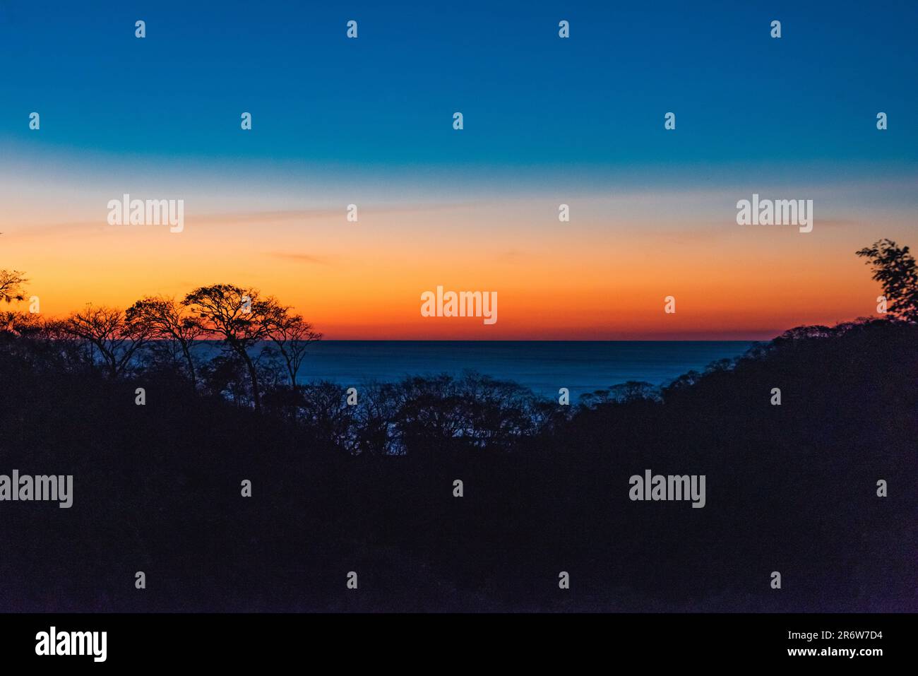 Un spectaculaire coucher de soleil bleu et orange surplombant l'océan pacifique au-dessus de la canopée de la jungle pendant la saison sèche au Nicaragua près de San Juan del sur Banque D'Images