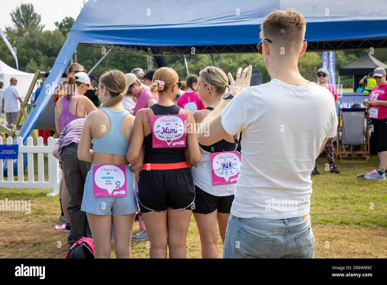 Warrington, Cheshire, Royaume-Uni. Dimanche 11 juin 2023 ; Warrington, Cheshire, Royaume-Uni ; Race for Life in Victoria Park in AID of cancer Research. Des centaines de personnes habillées en rose ont participé à différents événements de collecte de fonds à l'aide de la recherche sur le cancer. Un homme prend une photo de trois filles qui ont un message sur le dos. Crédit : John Hopkins/Alamy Live News Banque D'Images