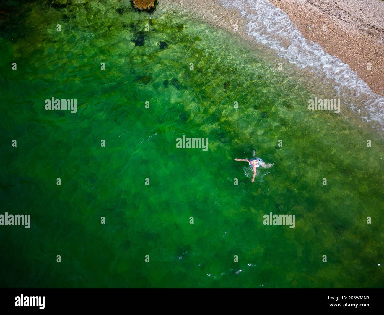 Femme se baignant et nageant sur la côte du Péloponnèse en eau verte et cristalline sur une plage romantique avec des rochers et une forêt en arrière-plan Banque D'Images