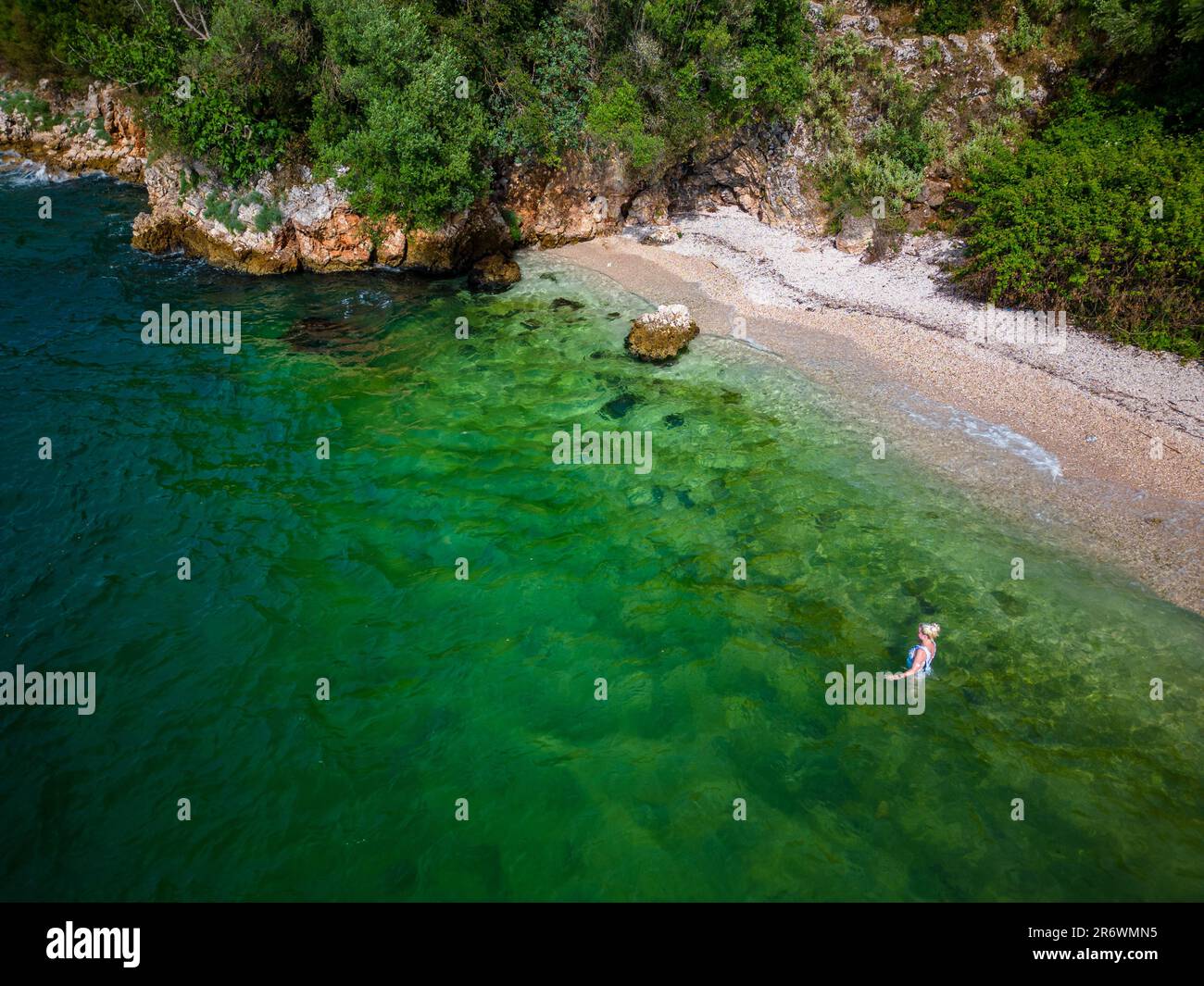 Femme se baignant et nageant sur la côte du Péloponnèse en eau verte et cristalline sur une plage romantique avec des rochers et une forêt en arrière-plan Banque D'Images