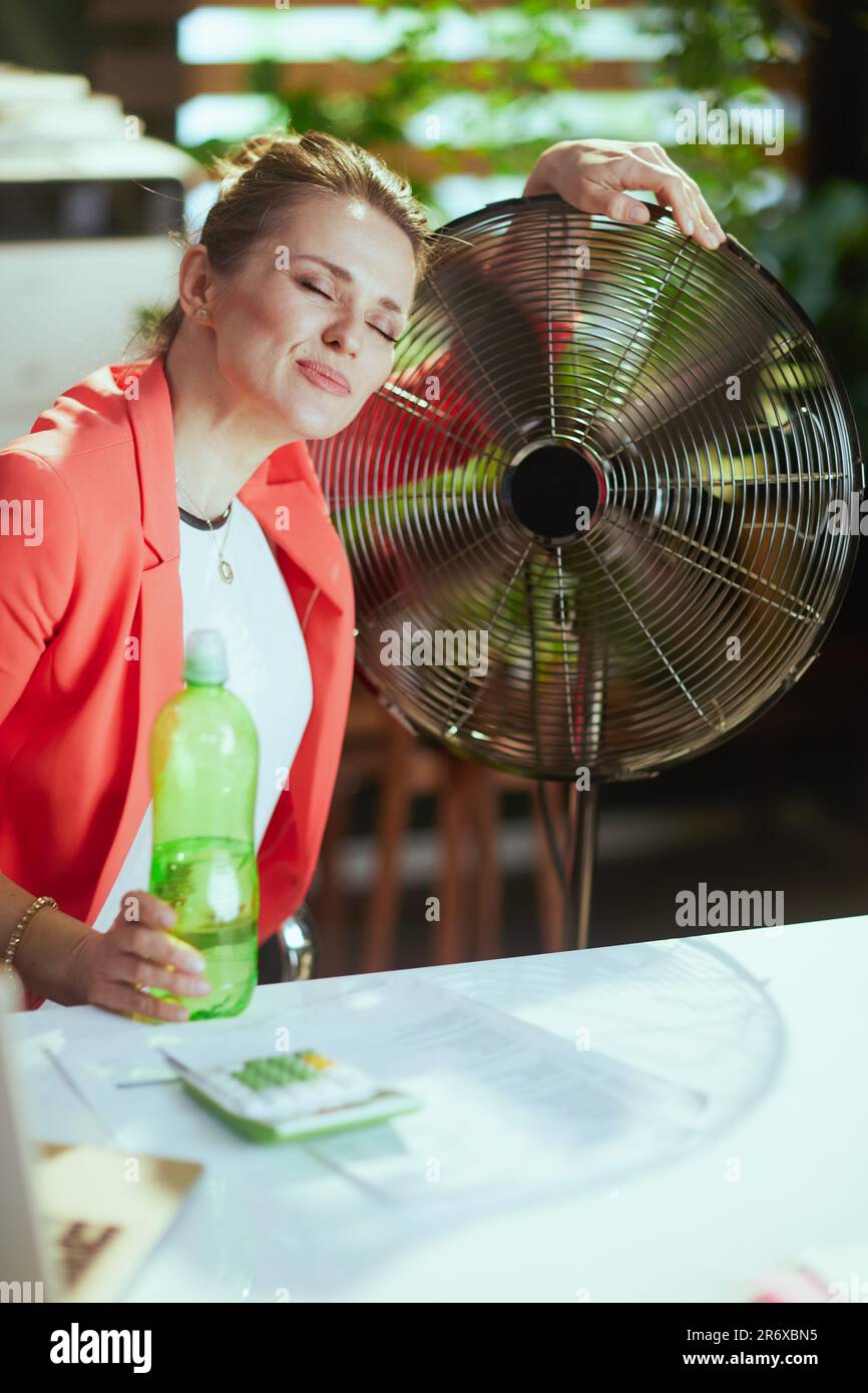 Un lieu de travail durable. femme d'affaires moderne souriante dans un  bureau moderne vert dans une veste rouge avec bouteille d'eau et ventilateur  électrique Photo Stock - Alamy