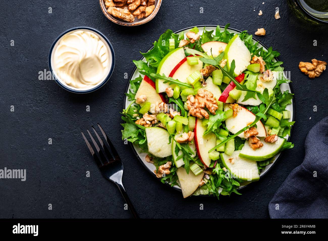 Salade Waldorf aux pommes rouges et vertes, céleri cru, laitue, arugula et noix avec sauce mayonnaise, fond de table noir, vue du dessus Banque D'Images