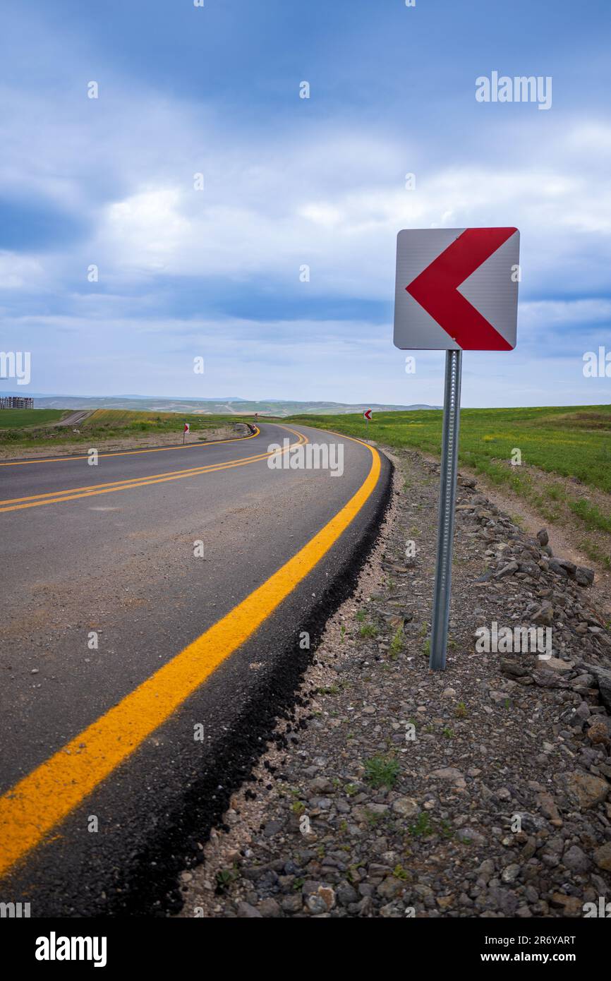 Route sinueuse de haute qualité nouvellement pavée avec lignes jaunes et panneau de virage Banque D'Images