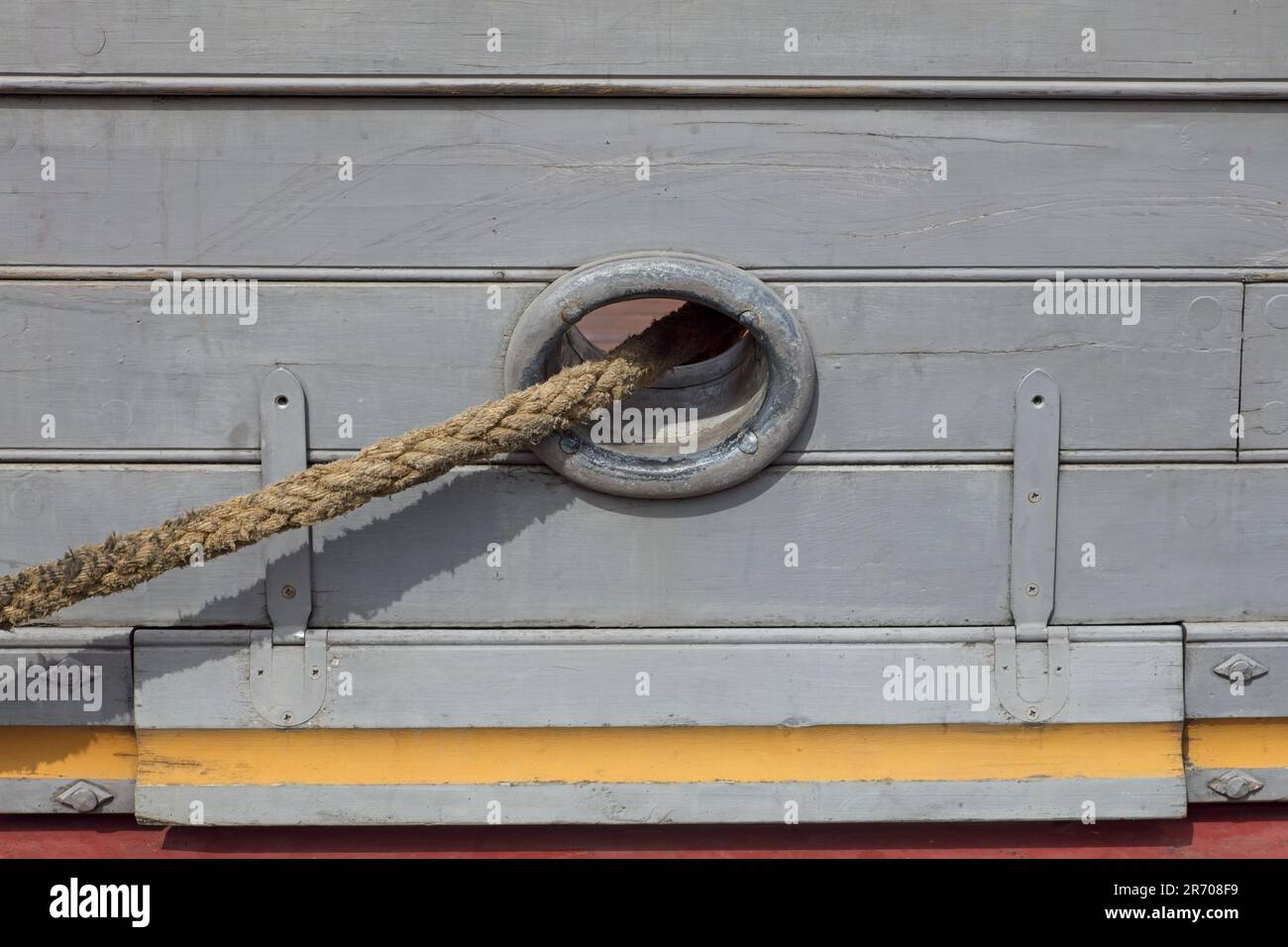 Une corde d'amarrage sortant du trou sur le côté d'un vieux navire en bois. Banque D'Images