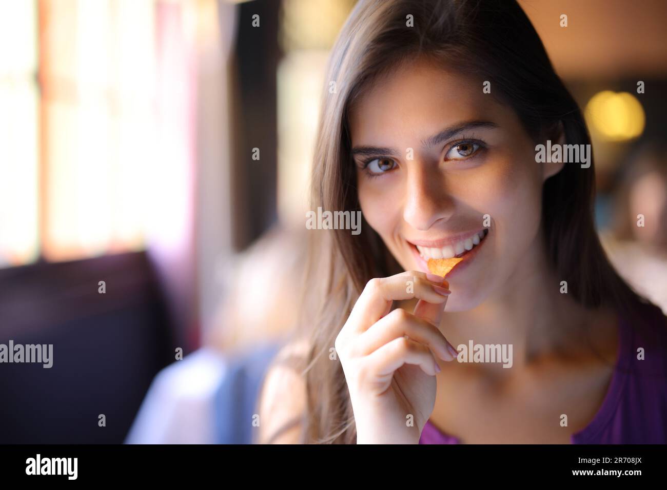 Une femme heureuse dans un restaurant qui mange des frites et qui vous regarde Banque D'Images