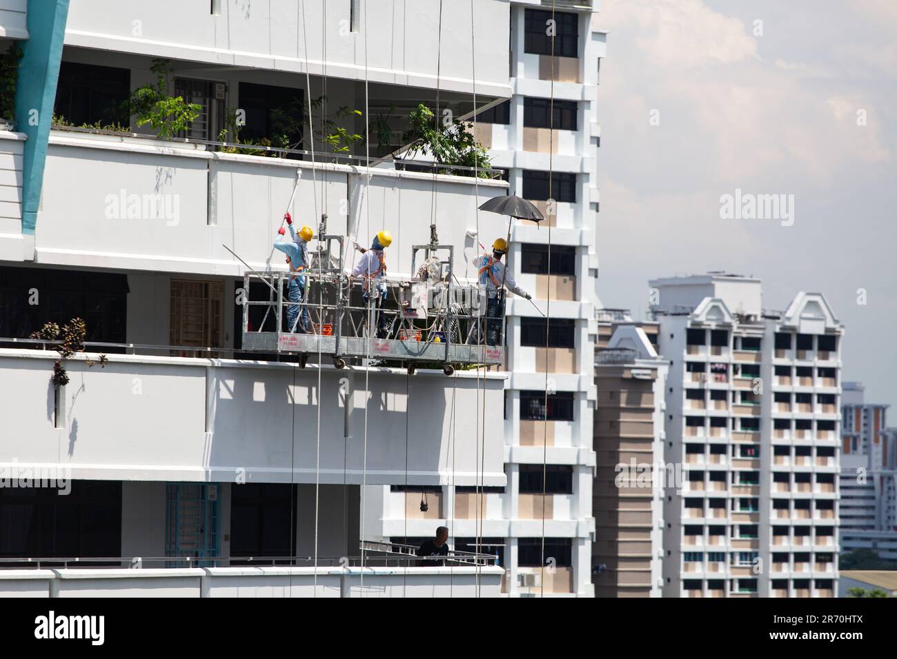 Les travailleurs utilisant un ascenseur industriel suspendu en plein air font un travail de peinture pour un bâtiment extérieur sous le soleil brûlant. Une profession à très haut risque. Banque D'Images