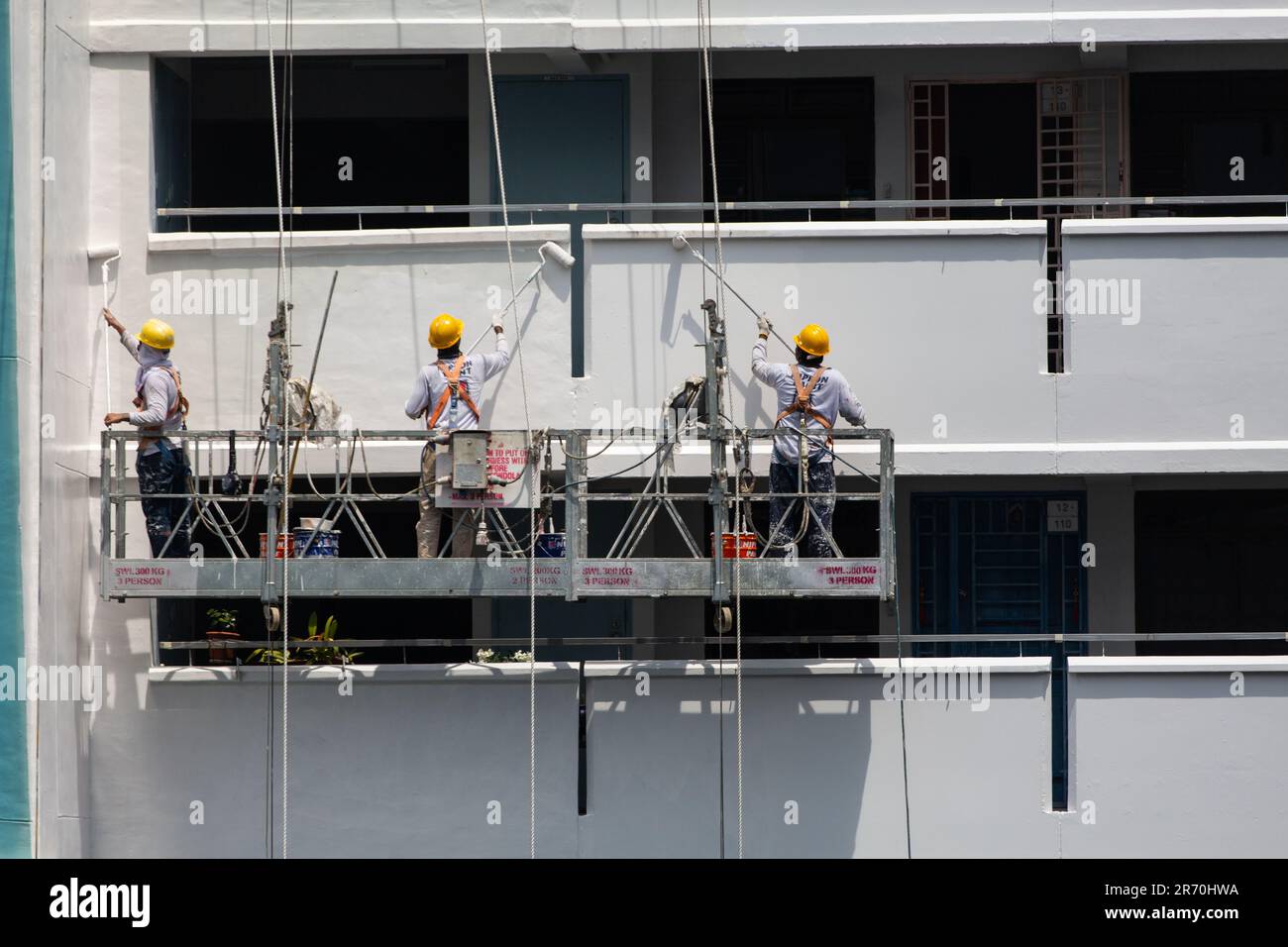 Les travailleurs utilisant un ascenseur industriel suspendu en plein air font un travail de peinture pour un bâtiment extérieur sous le soleil brûlant. Une profession à très haut risque. Banque D'Images