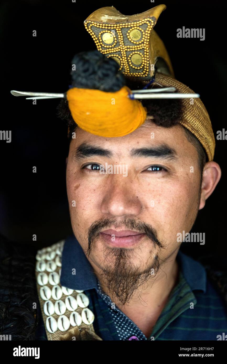Portrait d'un Nyishi dans ses vêtements tribaux traditionnels avec chapeau de cérémonie sur sa tête dans sa maison traditionnelle, Arunachal Pradesh, Inde Banque D'Images