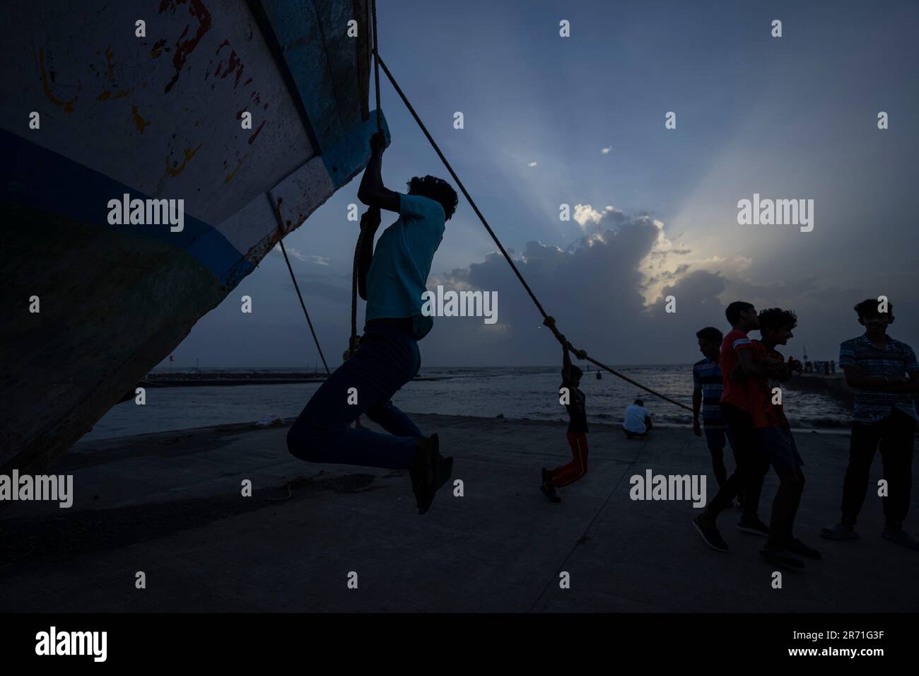 Cyclone Rope Boys play with the ropes of an anchored fishing boat as high tide waves ...