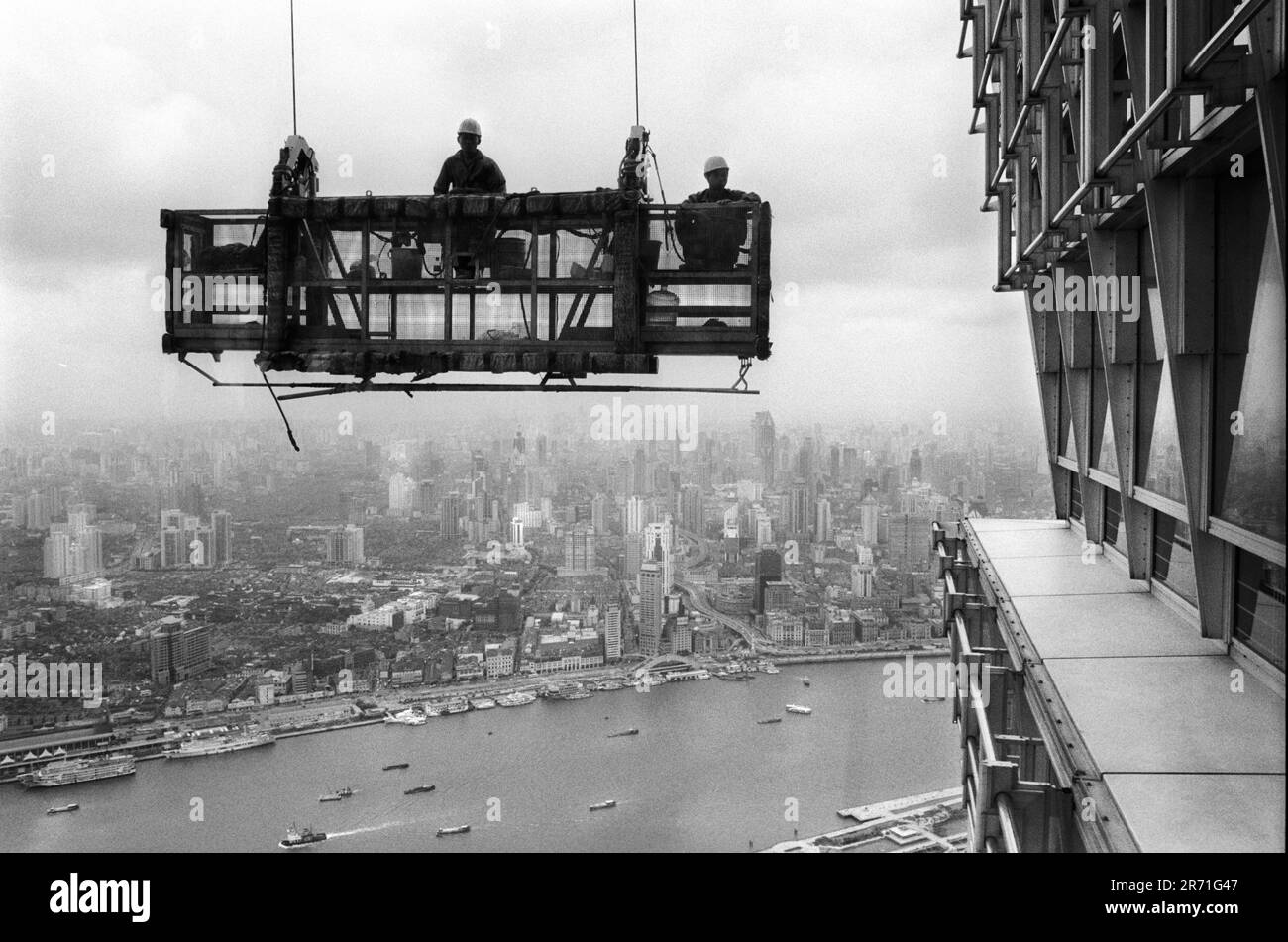 Shanghai Chine 2000. Les nettoyeurs de fenêtre obtiennent un ascenseur au sommet du bâtiment Jin Mao à Pudong. L'autoroute en hauteur de Yan et Zhong lu peut être vu en descendant jusqu'au Bund, tandis que la zone sombre à gauche est le site de la vieille ville chinoise connue sous le nom de Nanshi. 2000s HOMER SYKES Banque D'Images