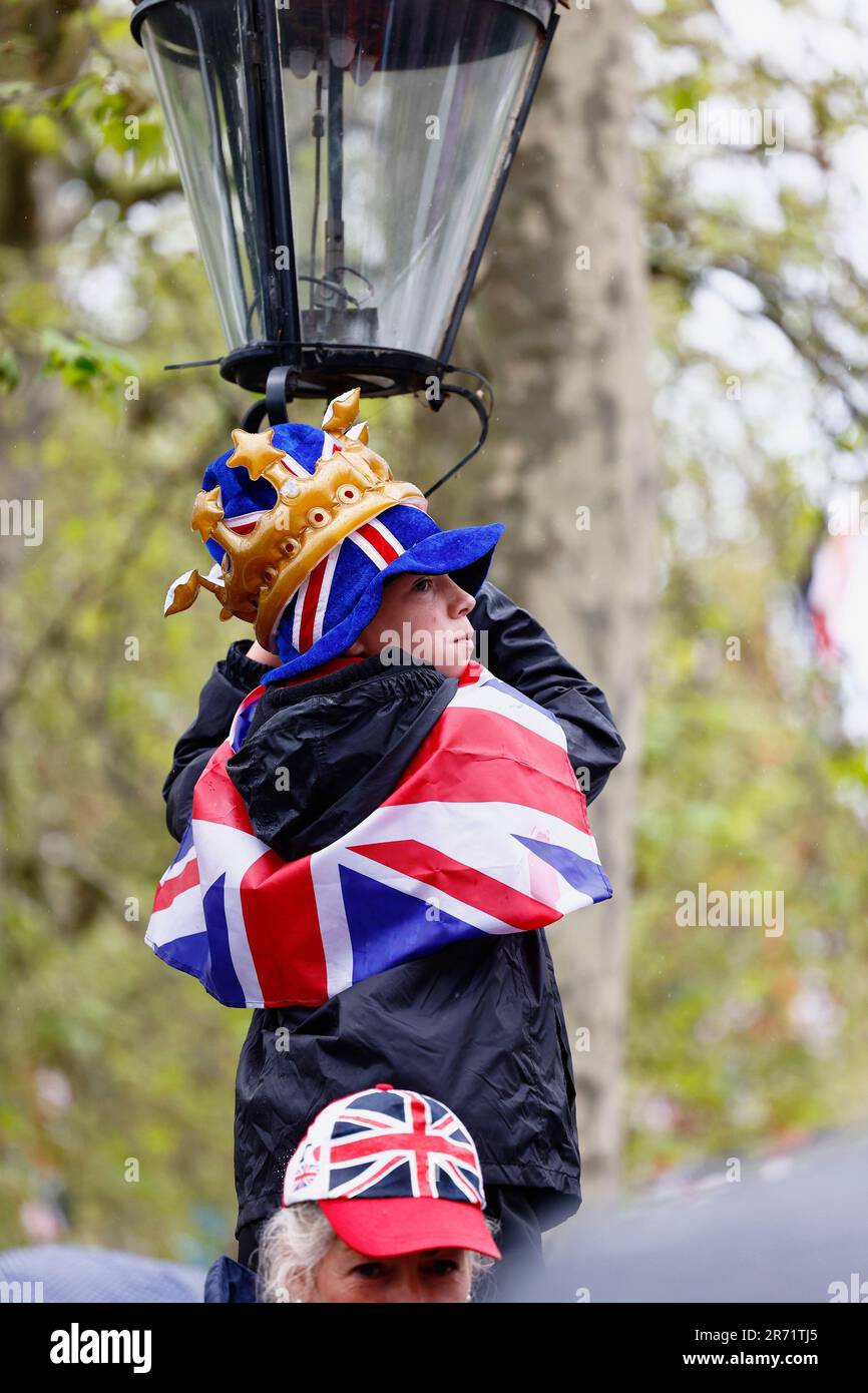 Angleterre, Londres, le centre commercial, la lampe d'escalade de jeune garçon pour obtenir une meilleure vue sur le couronnement du roi Charles III sur un 6 mai 2023 pluvieux. Banque D'Images