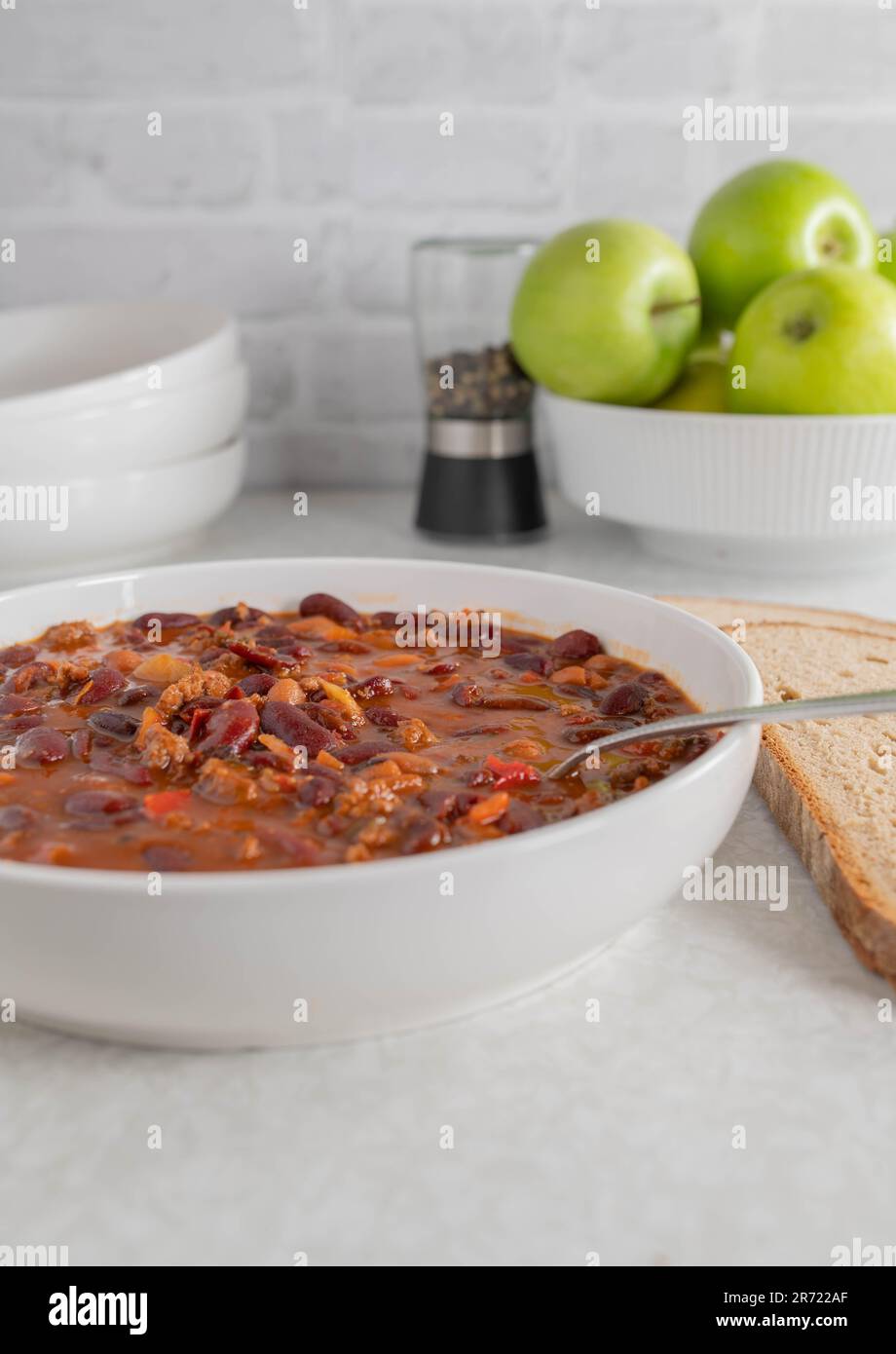 Ragoût de haricots avec du bœuf haché, des tomates, des poivrons, des oignons, de l'ail et des herbes sur une assiette avec une cuillère Banque D'Images