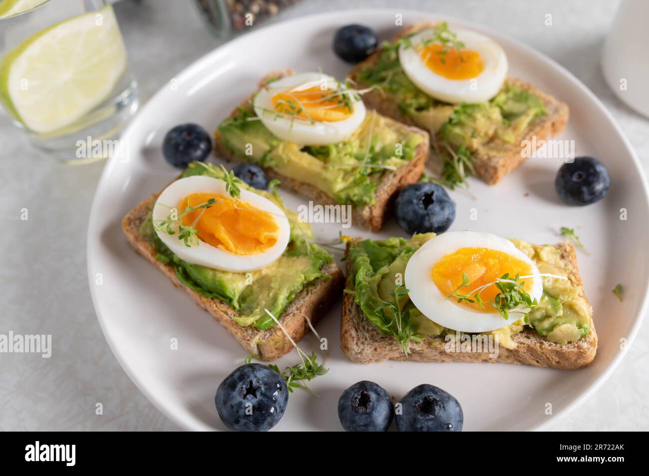 Pain grillé avec tartiner à l'avocat, œufs durs et cresson sur une assiette. Servi avec un verre d'eau et du café sur une table de cuisine. Banque D'Images