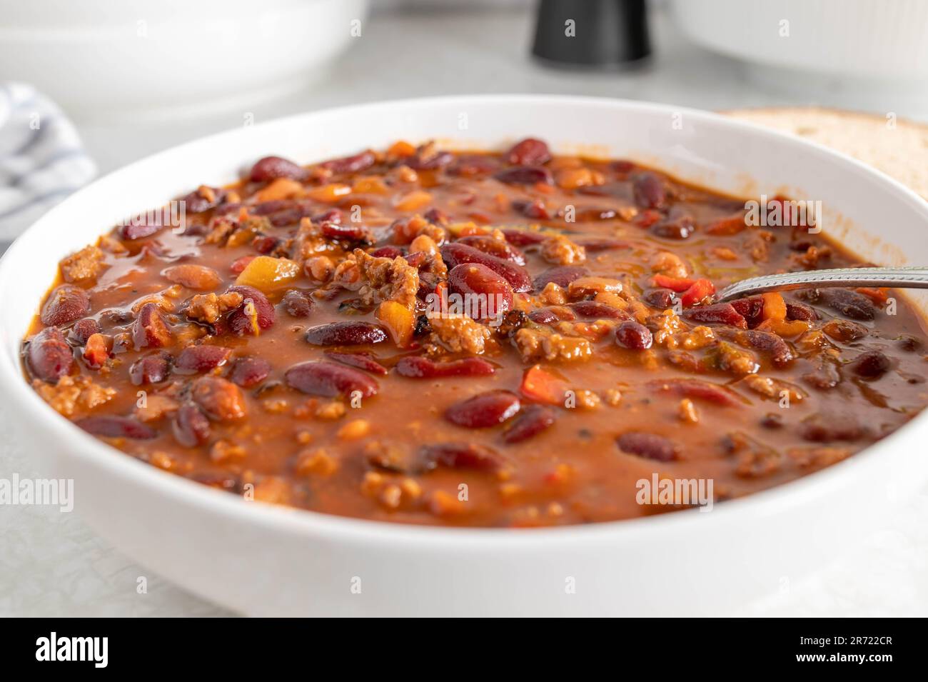 Ragoût de haricots avec du bœuf haché, des tomates, des poivrons, des oignons, de l'ail et des herbes sur une assiette avec une cuillère Banque D'Images
