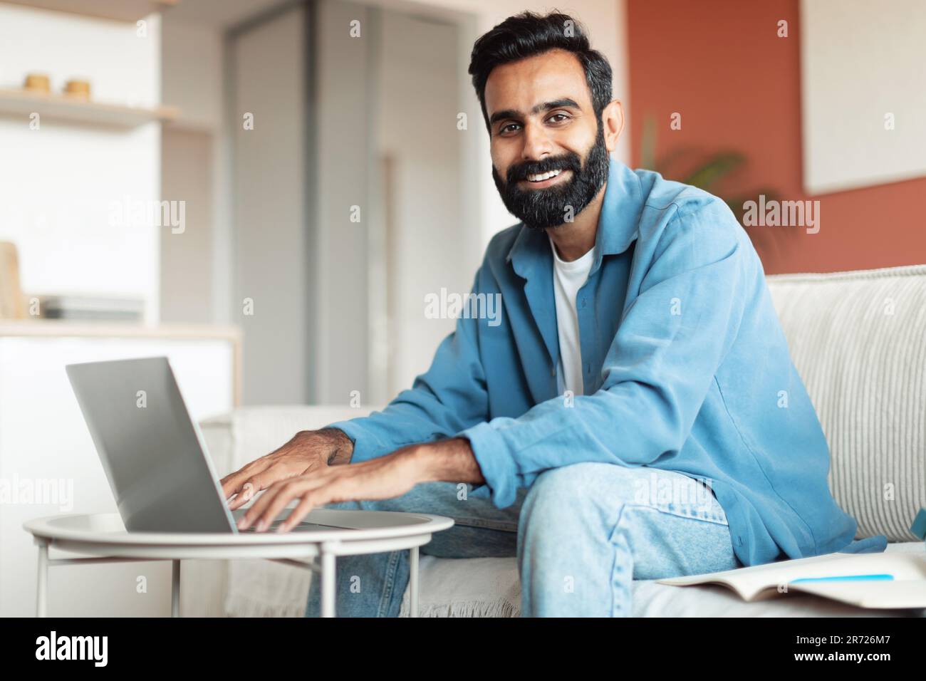 Homme arabe souriant travaillant sur un ordinateur portable assis dans le salon Banque D'Images