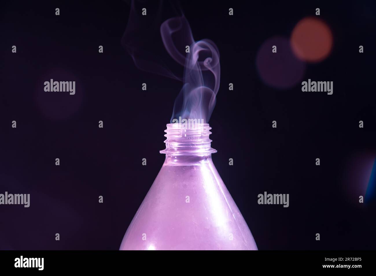 Une bouteille en plastique avec son couvercle éteint émet un panache de fumée dans l'air sur fond sombre Banque D'Images