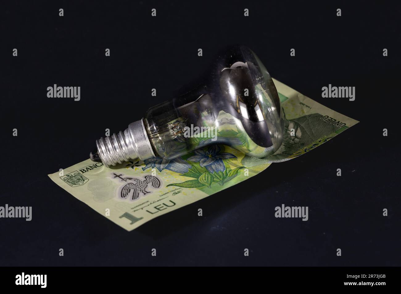 Photo d'un billet de 1 leu reposant sur une ampoule utilisée pour montrer l'augmentation des prix de l'électricité en Roumanie. Banque D'Images