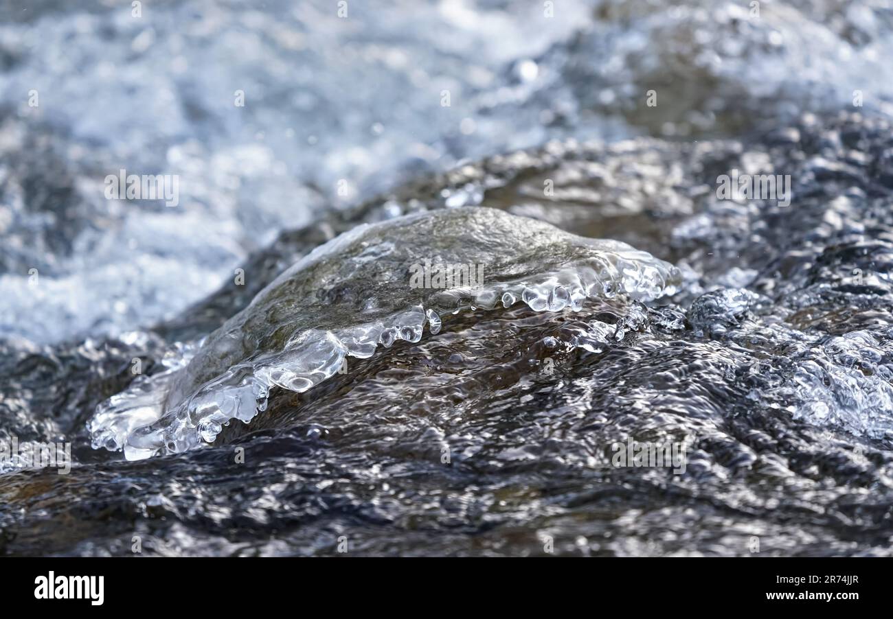 L'eau de la rivière coule près de la pierre recouverte de glace, détail gros plan Banque D'Images