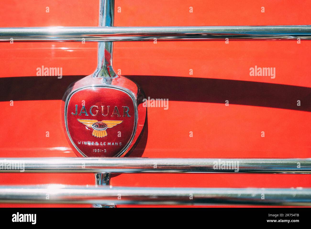 Séville, Espagne - 12 avril 2023 : vainqueur de la Jaguar 1951-3 le Mans rouge logo auto britannique sur le fond rouge de la vieille voiture vintage avec des barres chromées en S. Banque D'Images