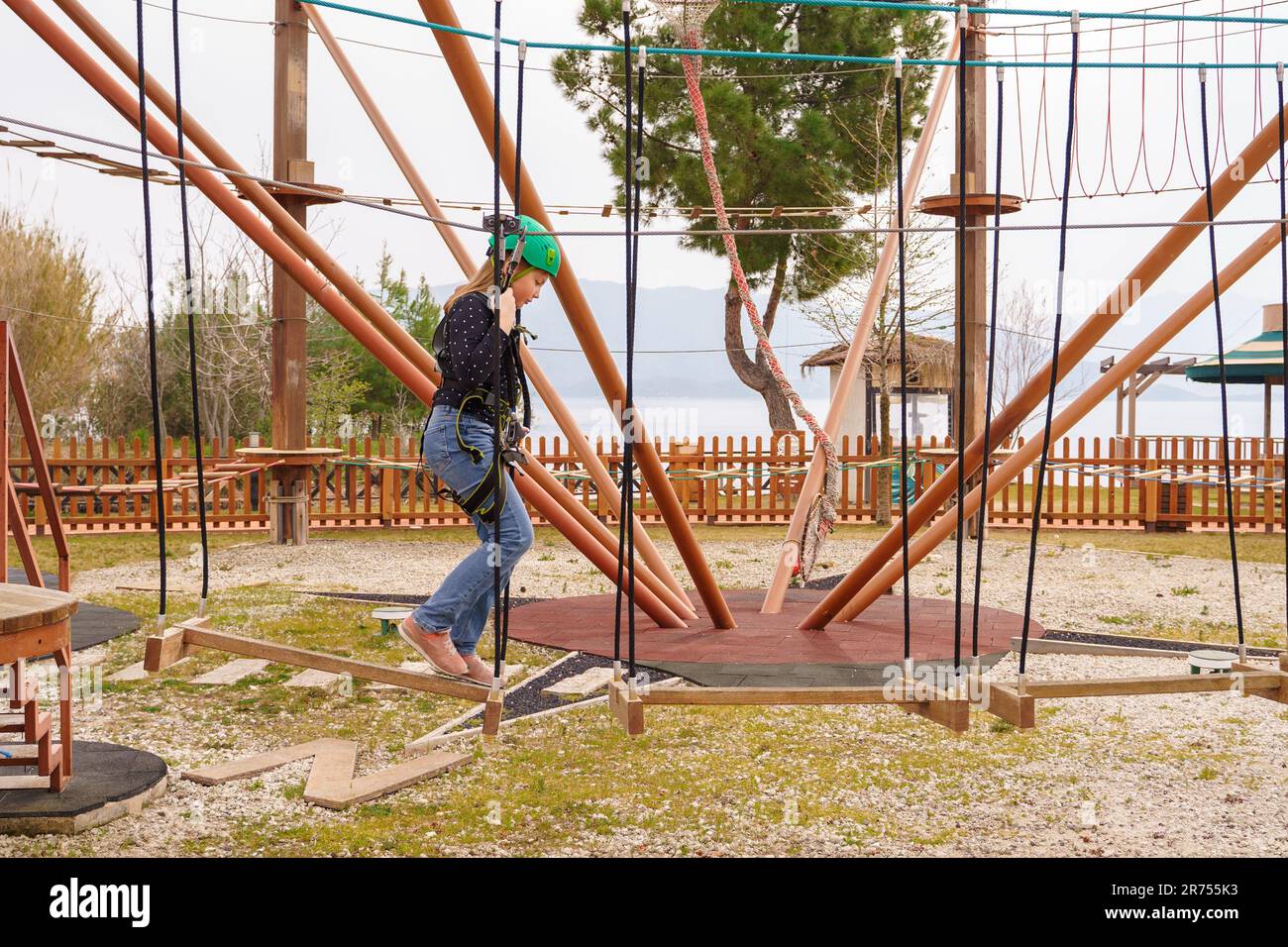 Adolescente dans l'équipement de harnais d'escalade, casque de sécurité vert de sport. Parc d'attractions de corde. Fixation fixant le mousqueton à la corde de sécurité. Hangin Banque D'Images