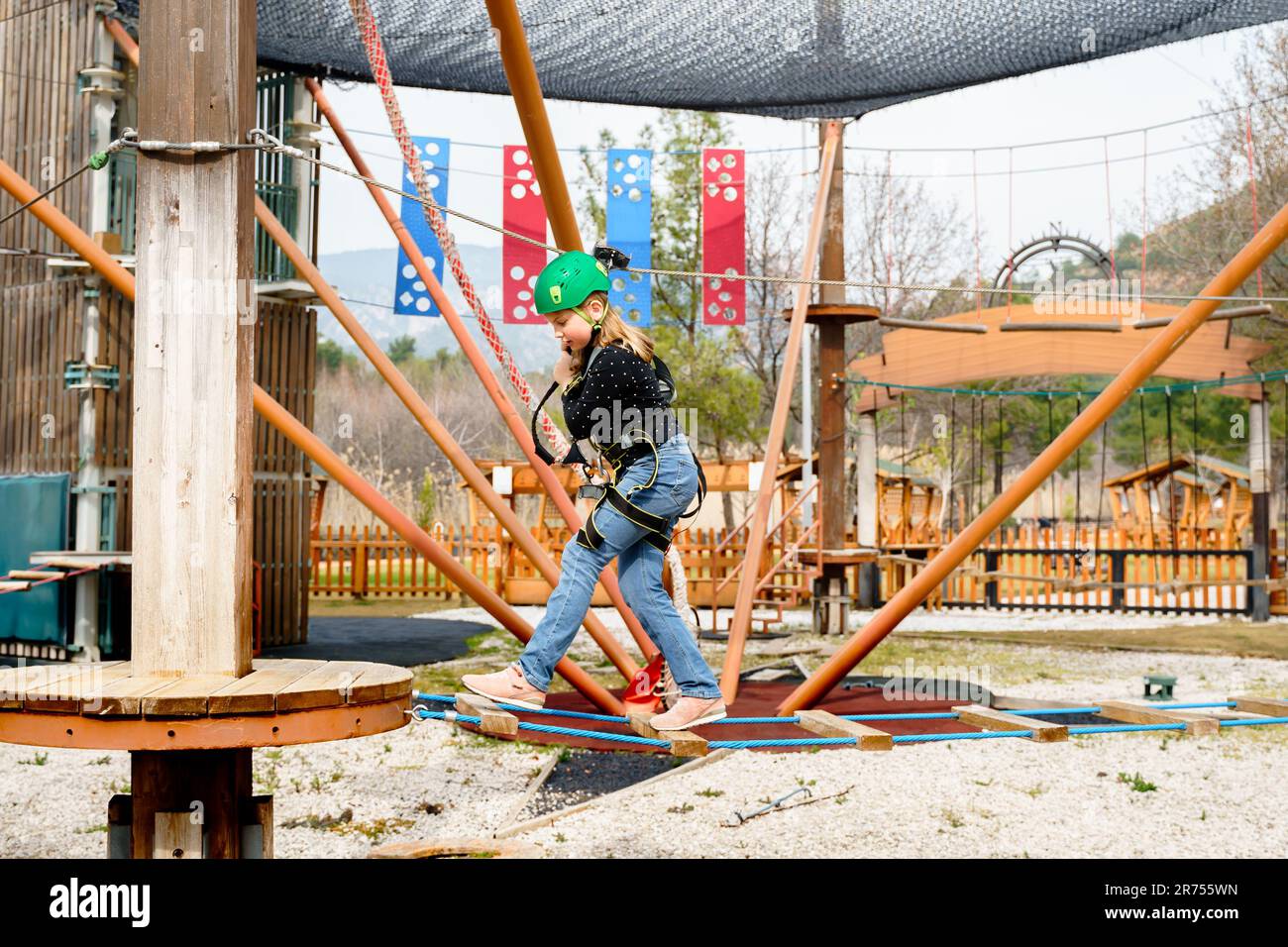 Adolescente dans l'équipement de harnais d'escalade, casque de sécurité vert de sport. Parc d'attractions de corde. Fixation fixant le mousqueton à la corde de sécurité. Hangin Banque D'Images