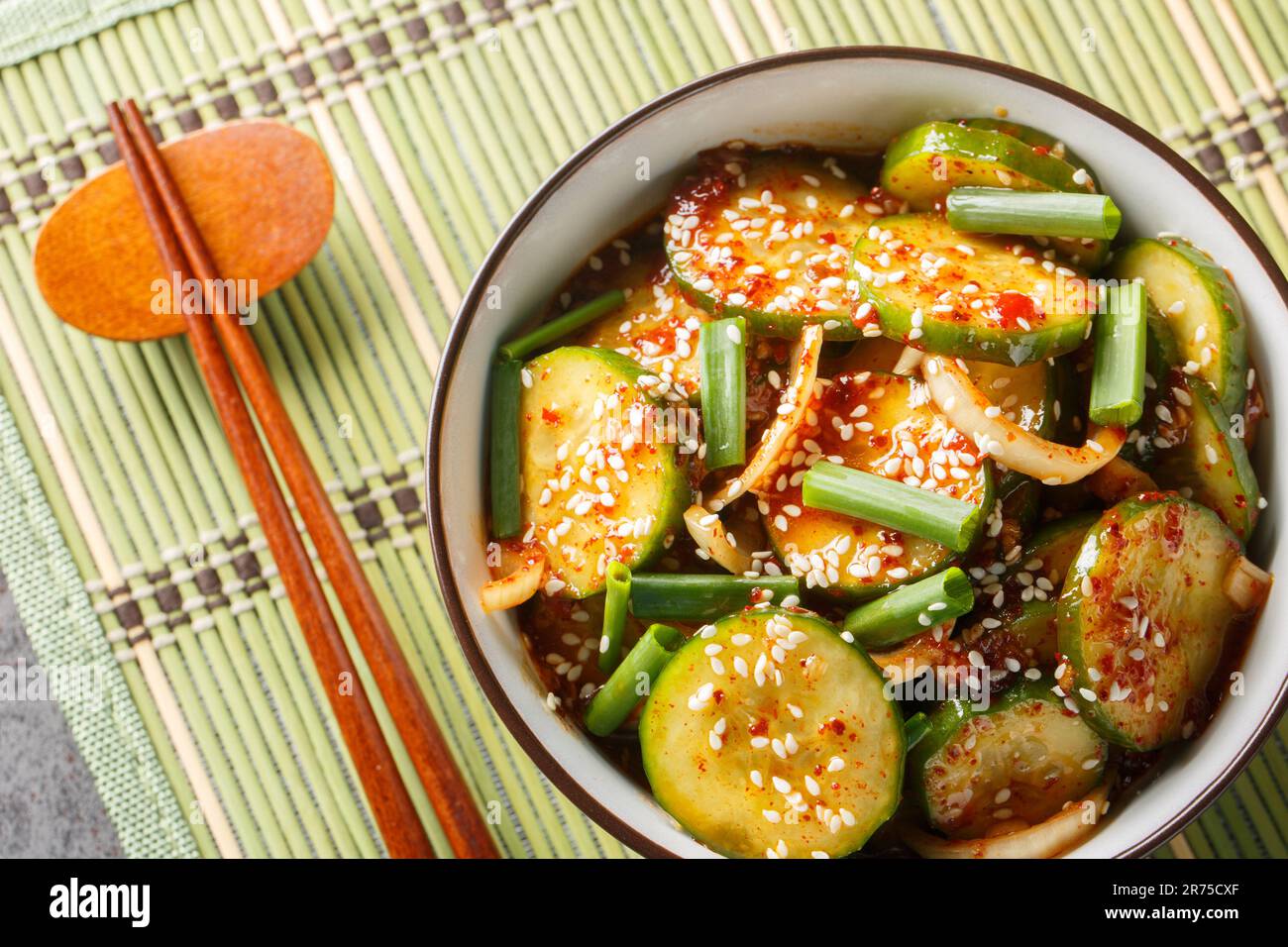 Salade de concombre coréen épicée à la sauce kimchi avec graines de sésame dans un bol avec baguettes sur la table. Vue horizontale du dessus Banque D'Images