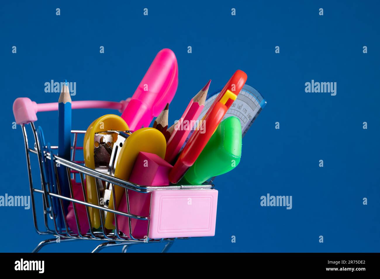Gros plan d'un petit chariot de magasinage avec matériel scolaire et espace de copie sur fond bleu. Retour à l'école, shopping, matériel scolaire, apprentissage, Banque D'Images