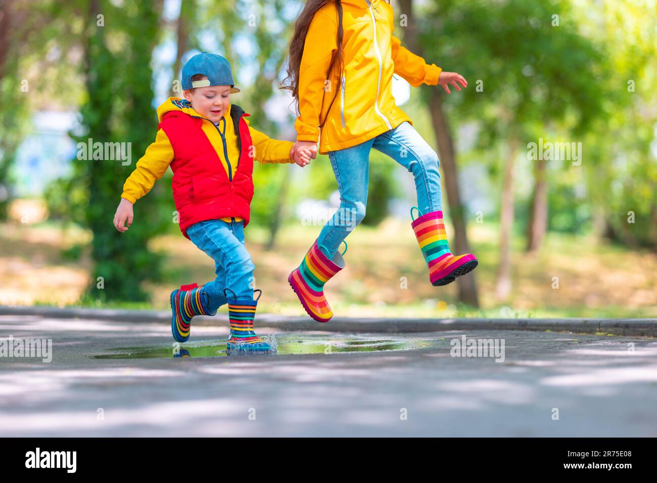 Joyeux enfant fille et garçon avec parapluie et caoutchouc coloré bottes de pluie jouant à l'extérieur et sautant dans la flaque de pluie Banque D'Images