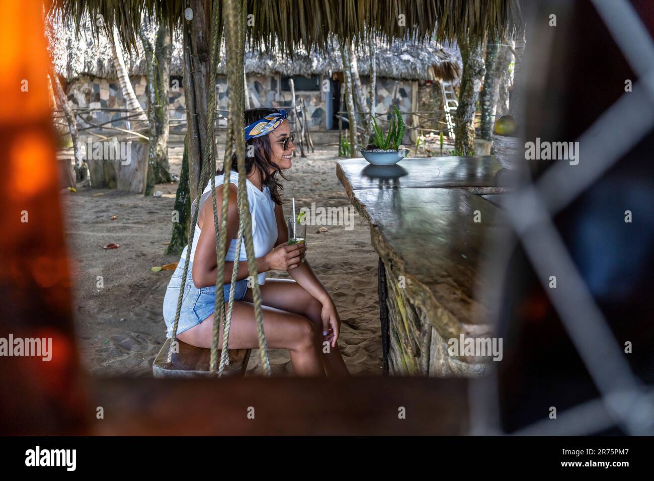 Amérique du Nord, Caraïbes, Grande Antilles, Île d'Hispaniola, République dominicaine, Côte Nord, province de Puerto Plata, Cabarete, Natura Cabana, belle Latina se trouve sur Une balançoire au bar de la plage ayant Un verre Banque D'Images