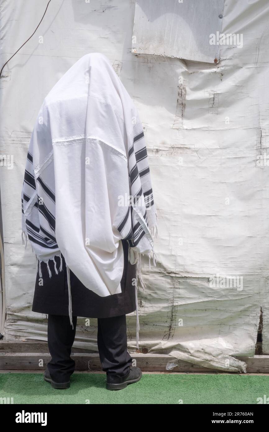 Un juif plus âgé non identifié récite des prières matinales avec un tallis au-dessus de sa tête devant une tente dans un complexe de synagogue de Monsey, New York, 2023. Banque D'Images