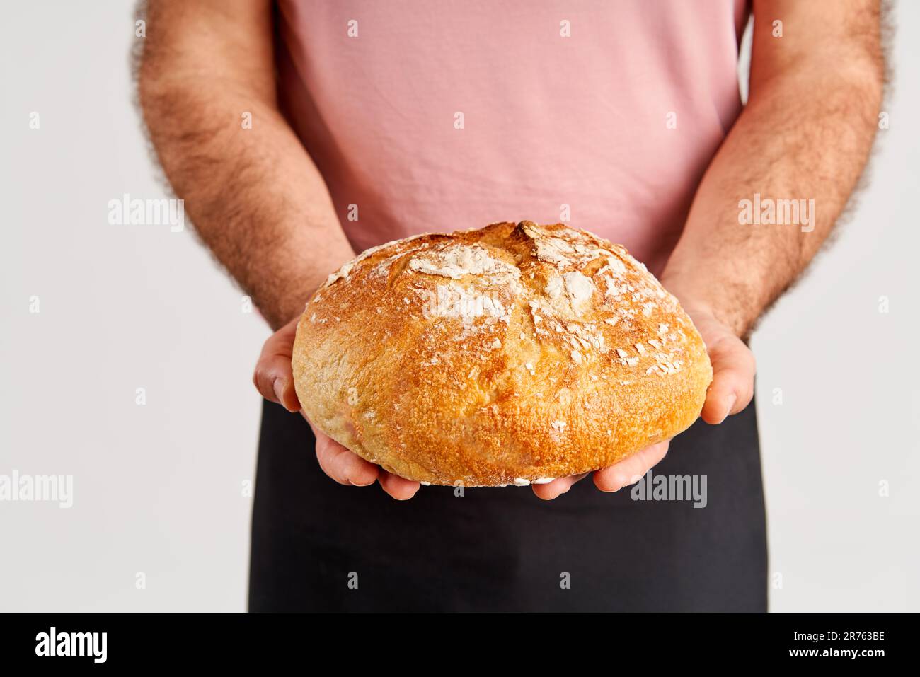 Baker dans un tablier tenant le pain de pain frais cuit dans les mains. Boulangerie, concept alimentaire Banque D'Images