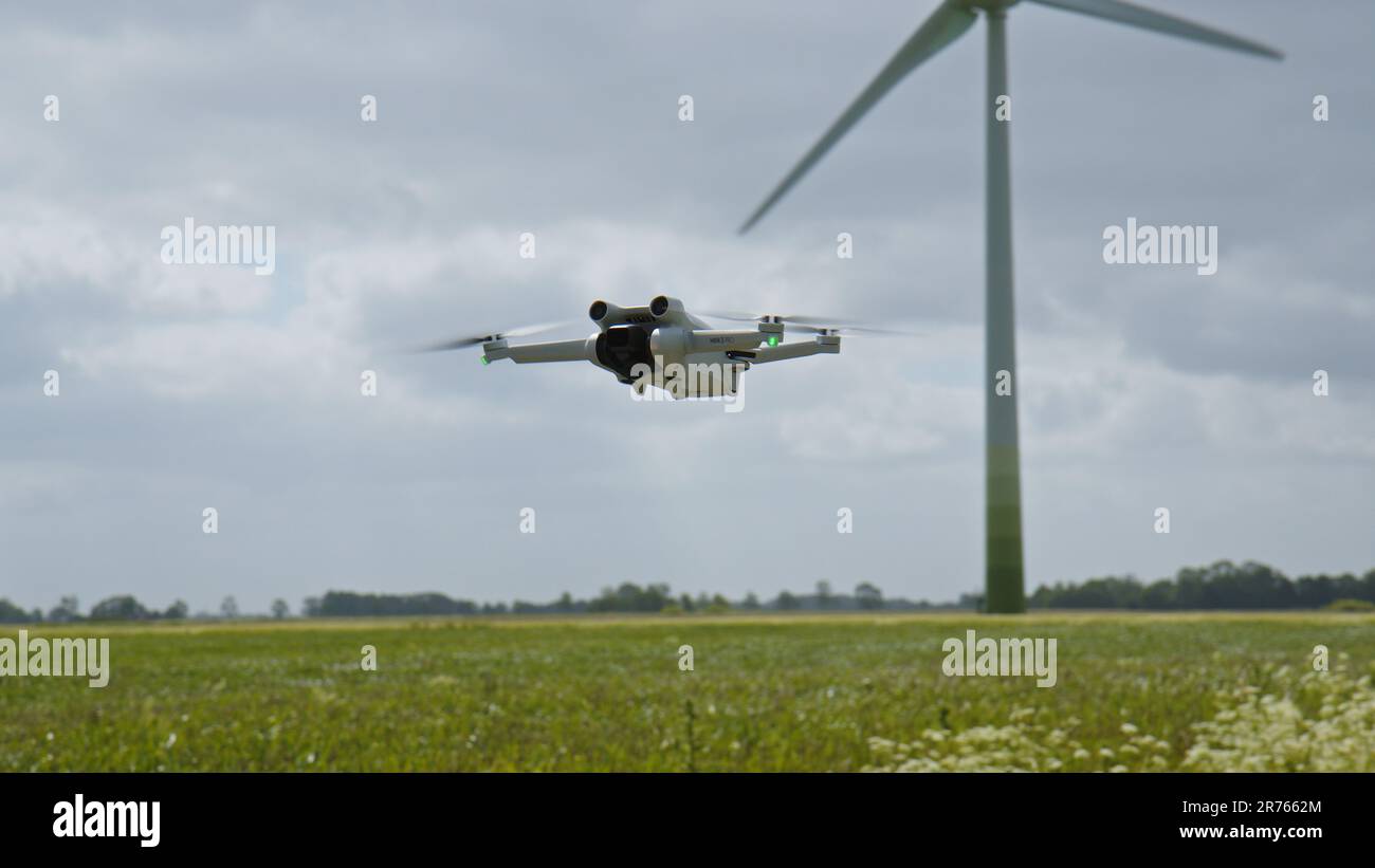 FRISE ORIENTALE, ALLEMAGNE - 25 MAI 2023: Caméra Drone DJI Mini 3 Pro planant dans l'air près d'un champ avec des éoliennes Banque D'Images
