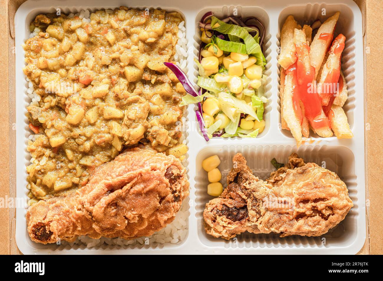 La boîte à bento contient du riz au curry, des cuisses de poulet, des frites et de la salade de légumes. Banque D'Images