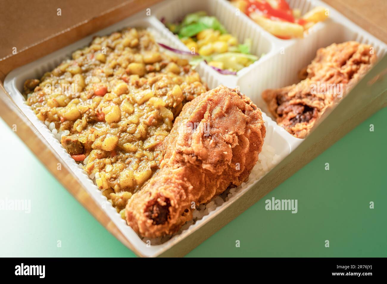 La boîte à bento contient du riz au curry, des cuisses de poulet, des frites et de la salade de légumes. Banque D'Images