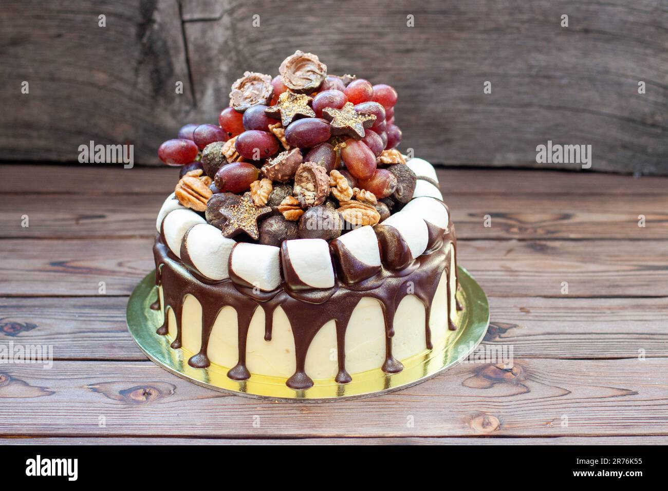 Gâteau d'automne fait de chocolat et décoré de raisins, de noix, de truffes au chocolat, de guimauves et d'étoiles. Fond rustique, cuisine de confort Banque D'Images