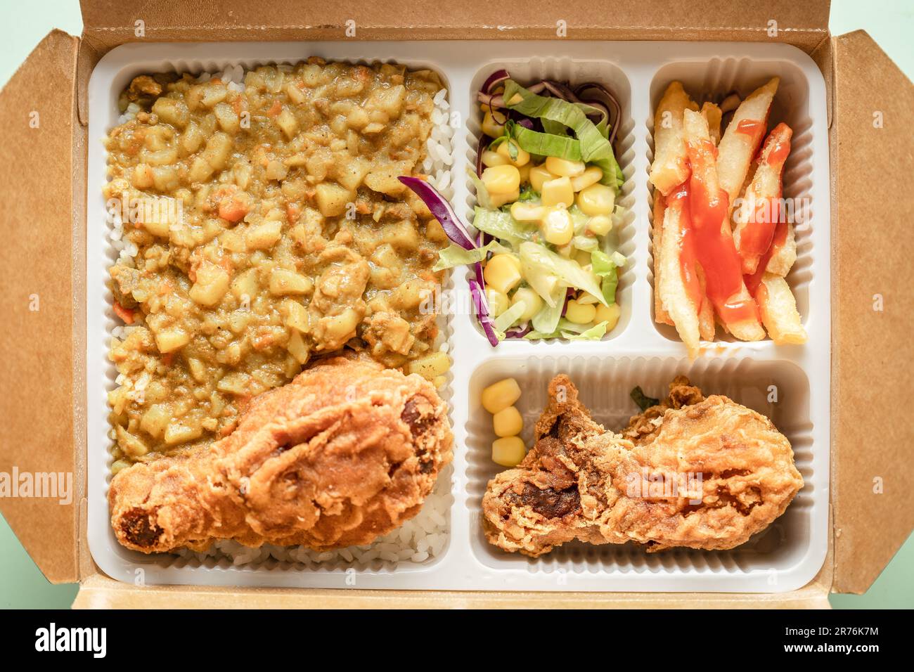 La boîte à bento contient du riz au curry, des cuisses de poulet, des frites et de la salade de légumes. Banque D'Images