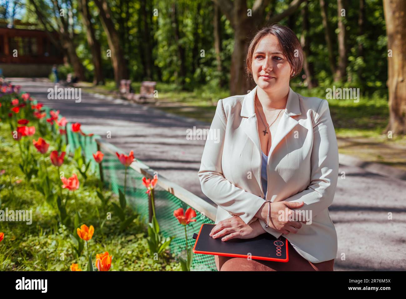 Portrait d'une femme d'affaires heureuse tenant une tablette dans un parc printanier. La paysagiste féminine bénéficie des résultats des massifs fleuris dans le Gard public Banque D'Images