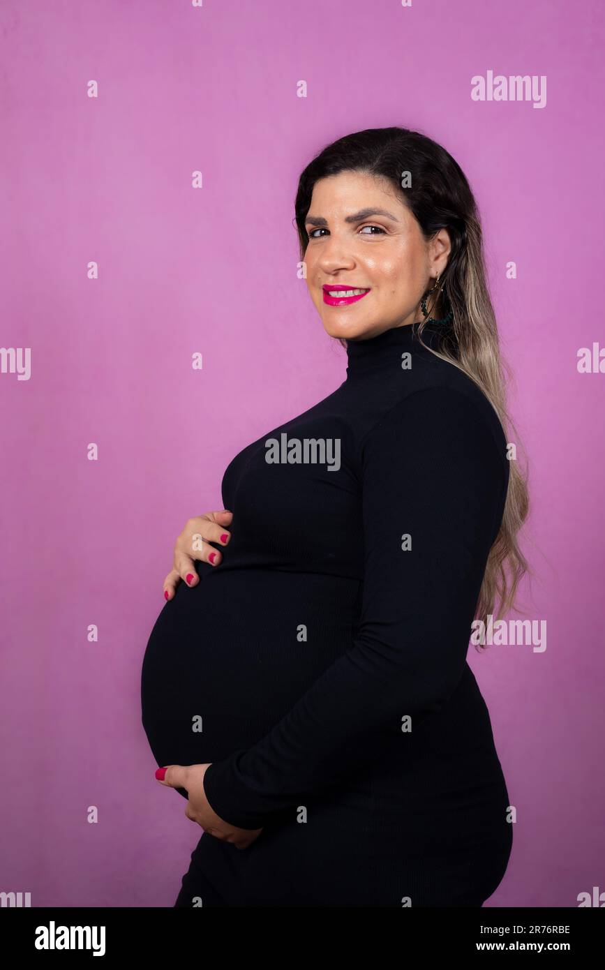 Une femme enceinte heureuse portant un haut noir à manches longues se tient sur un fond violet vif Banque D'Images