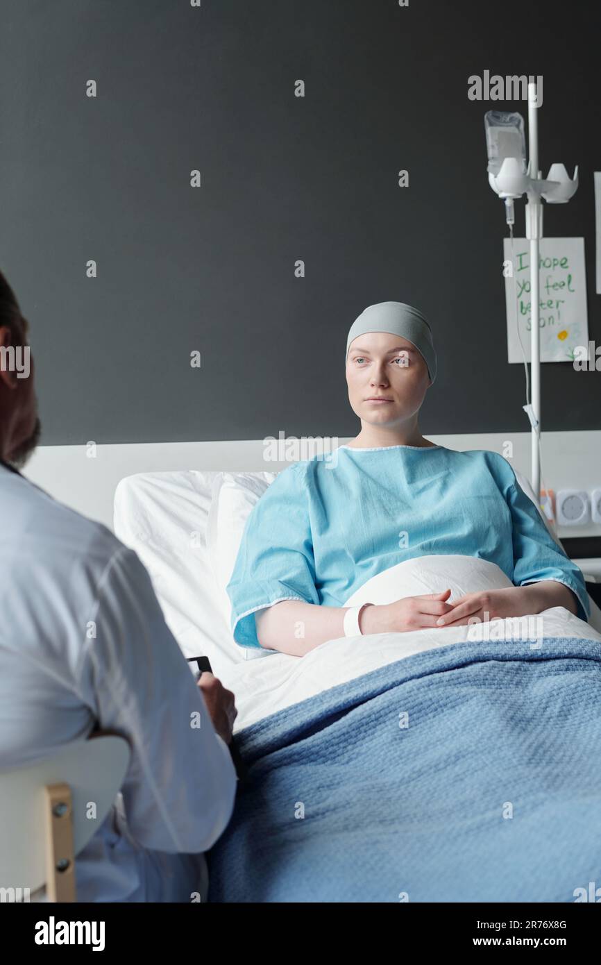 Jeune femme sérieuse en foulard regardant son médecin pendant la consultation  médicale tout en étant assise au lit devant lui dans les cliniques Photo  Stock - Alamy