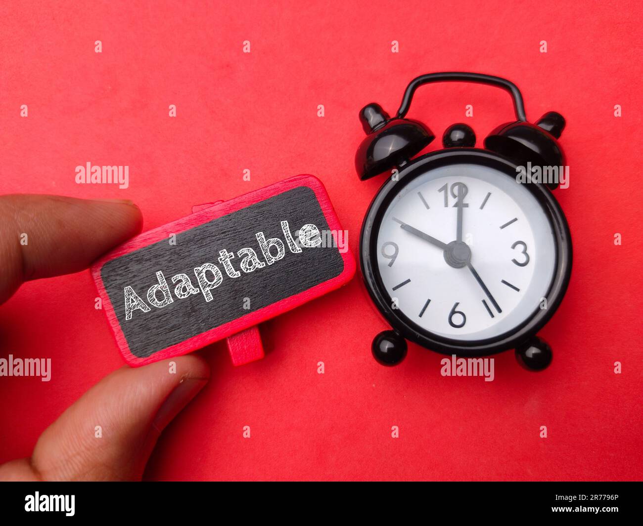 Un fond rouge avec un réveil et une main tenant un signe avec le mot adaptable Banque D'Images