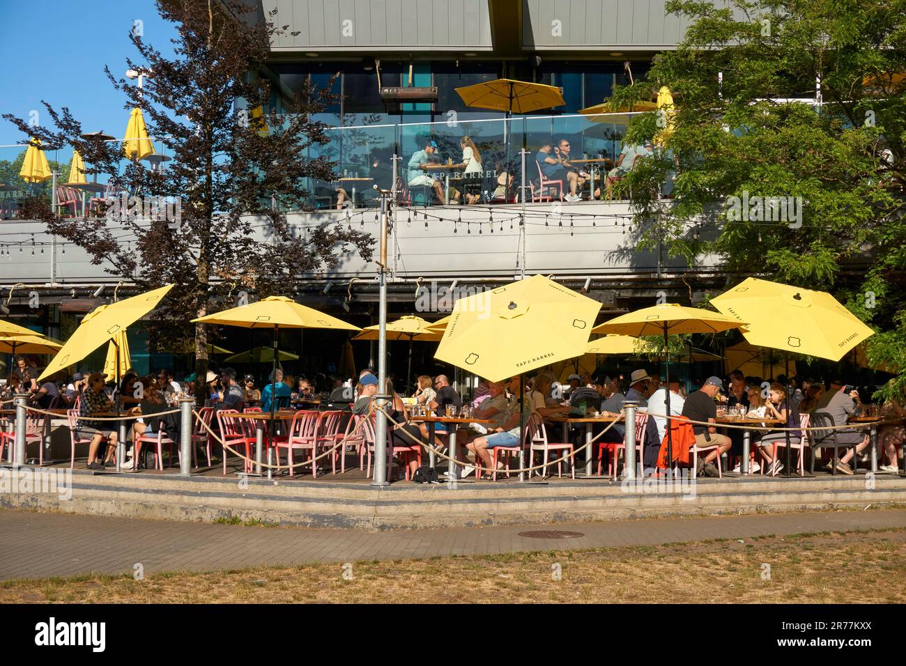 Des gens assis sur le bord de l'eau du robinet, un patio extérieur et le canon restaurant dans le village olympique, le False Creek, Vancouver, BC, Canada Banque D'Images