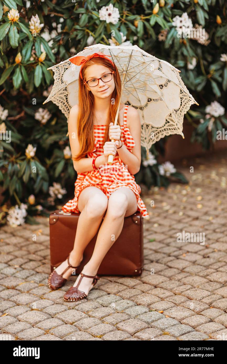 Portrait en plein air d'une petite fille drôle portant un combishort à  Vichy rouge, tenant un parasol en dentelle blanche, assis sur une vieille  valise rétro Photo Stock - Alamy